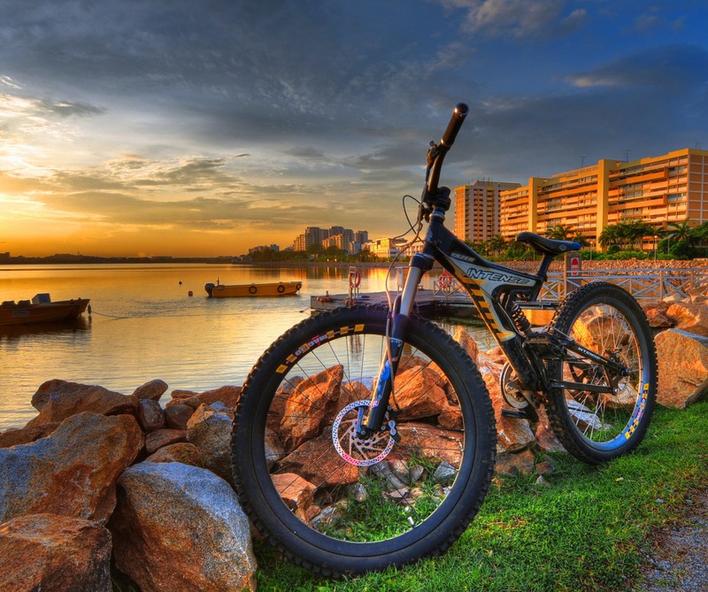 Arafed bike parked on a rock wall next to a body of water (bike, boats, city, cityscape, hd)