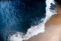 Aerial view of ocean waves gently lapping at a sandy seashore.