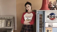 Shuhua de (G)I-DLE pose de manière stylée contre un fond rétro, mettant en valeur sa tenue vibrante et son charme ludique.