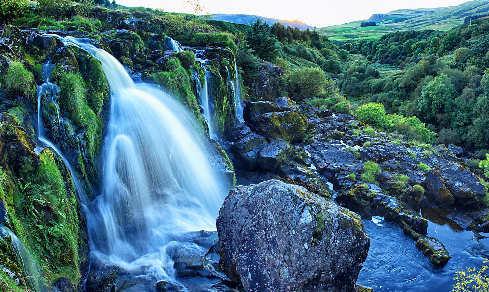 Cascada en medio de un valle con una gran roca en primer plano (cascada, recursos hídricos, cuerpo de agua, naturaleza, agua)