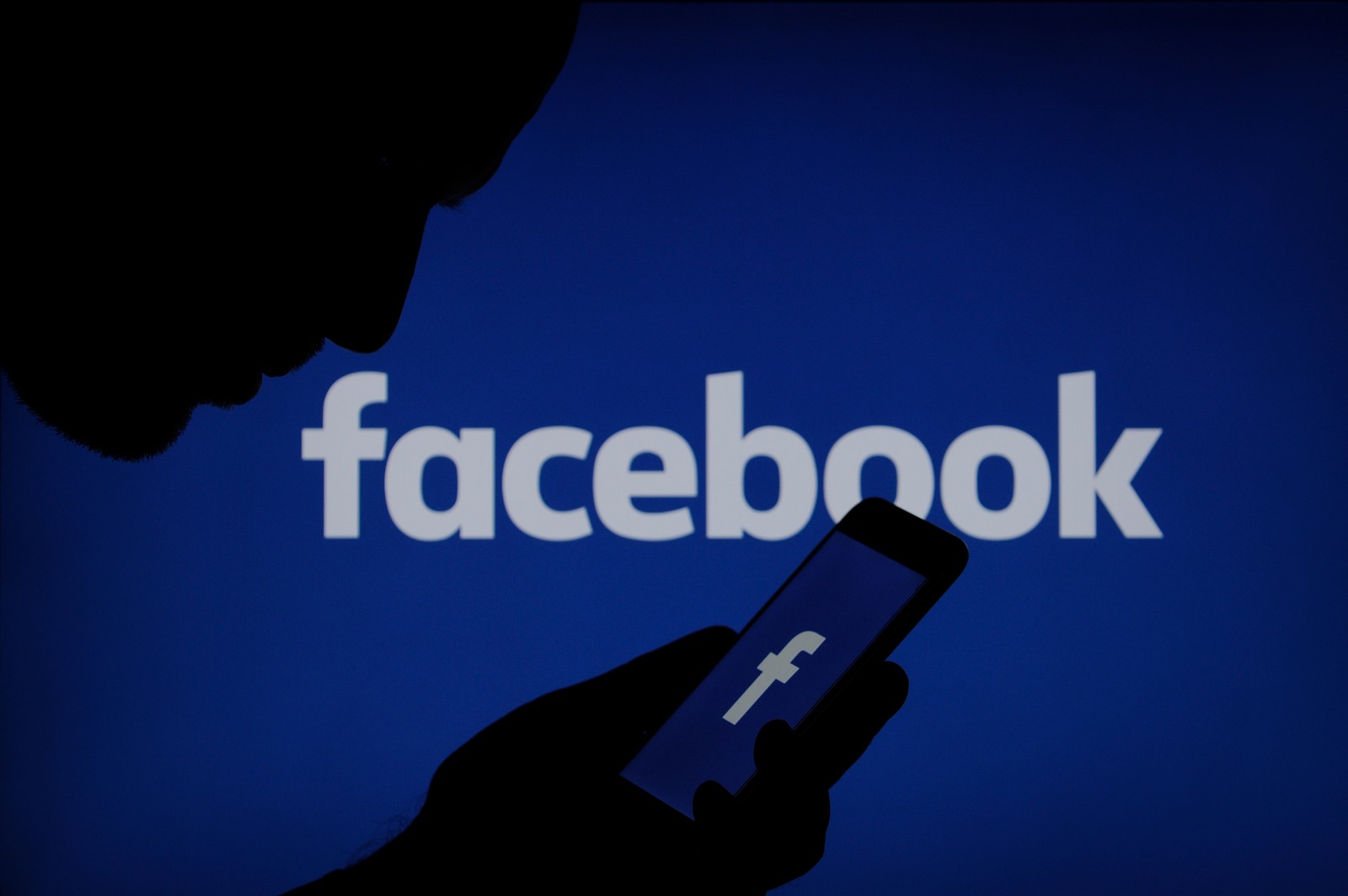 Imagem de um homem segurando um celular em frente ao logotipo do facebook (facebook, texto, azul, marca, logotipo)