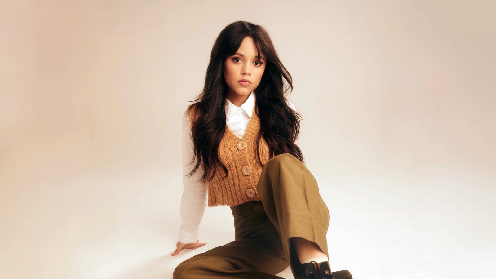 Un gros plan d'une femme assise sur un tabouret portant un pull et un pantalon (jenna ortega, célébrité, filles, femme, actrice)