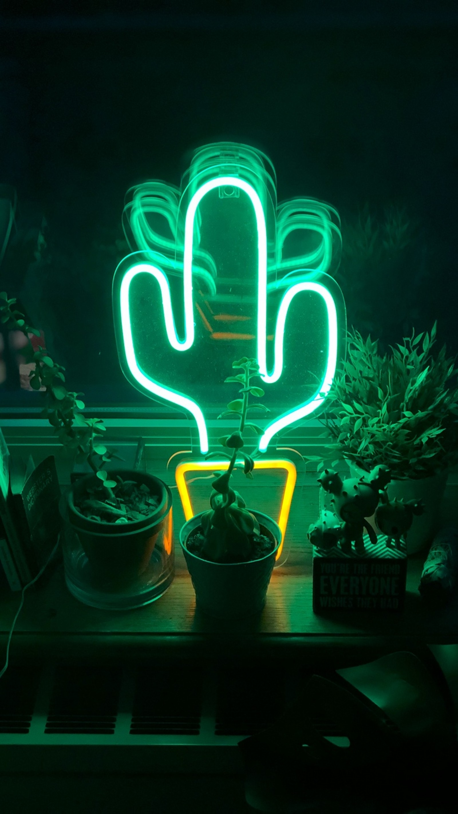 There is a neon cactus plant sitting on a table in front of a window (neon sign, neon lighting, neon, light, light emitting diode)