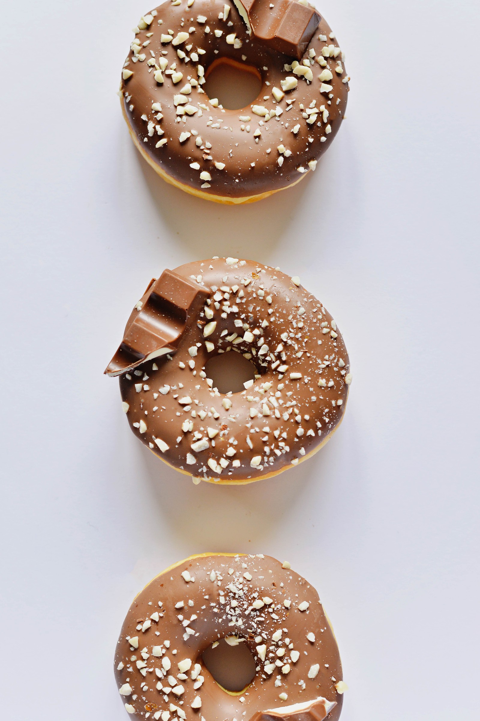 Tres donuts con chocolate y chispas sobre una superficie blanca (donut, chocolate, postre, glaseado, pastelería)