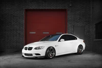 Elegante BMW M3 coupé blanco que muestra llantas de aleación personalizadas contra un fondo industrial rojo.