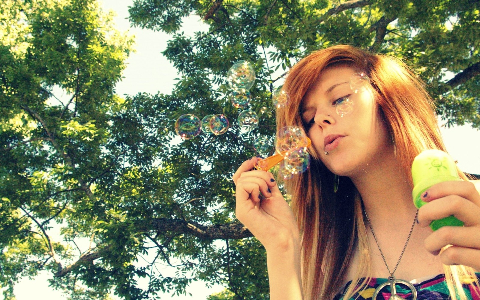 Araffe girl blowing bubbles in the park with a green bottle (soap bubble, soap, beauty, tree, sunlight)