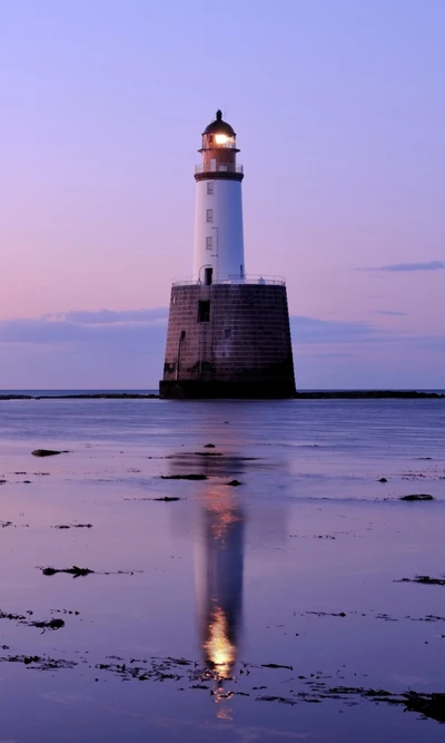 Reflejo del faro al anochecer en la playa serena