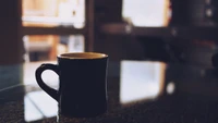 Caneca de café preta em uma mesa reflexiva em um ambiente aconchegante.