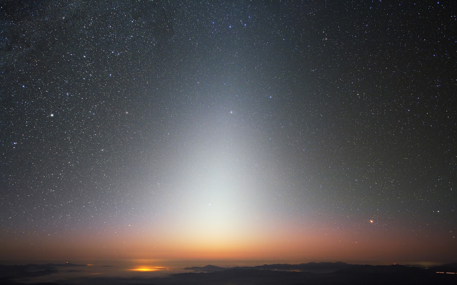 Uma vista de uma luz brilhante brilhando sobre uma cadeia de montanhas (astronomia, céu noturno, atmosfera, horizonte, objeto astronômico)