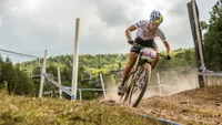 Dynamisches Abfahrts-Mountainbiking auf einem rauen Trail mit atemberaubenden grünen Hügeln im Hintergrund.