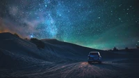 Un vehículo solitario bajo un impresionante cielo estrellado en un tranquilo paisaje desértico.