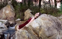 Serene Moment by the Creek: A Young Woman Relaxing on a Boulder