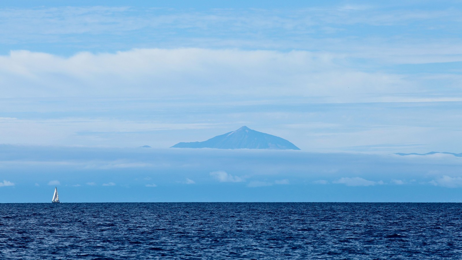 Vela arafed no oceano com uma montanha ao fundo (ilha, mar, horizonte, oceano, calmo)