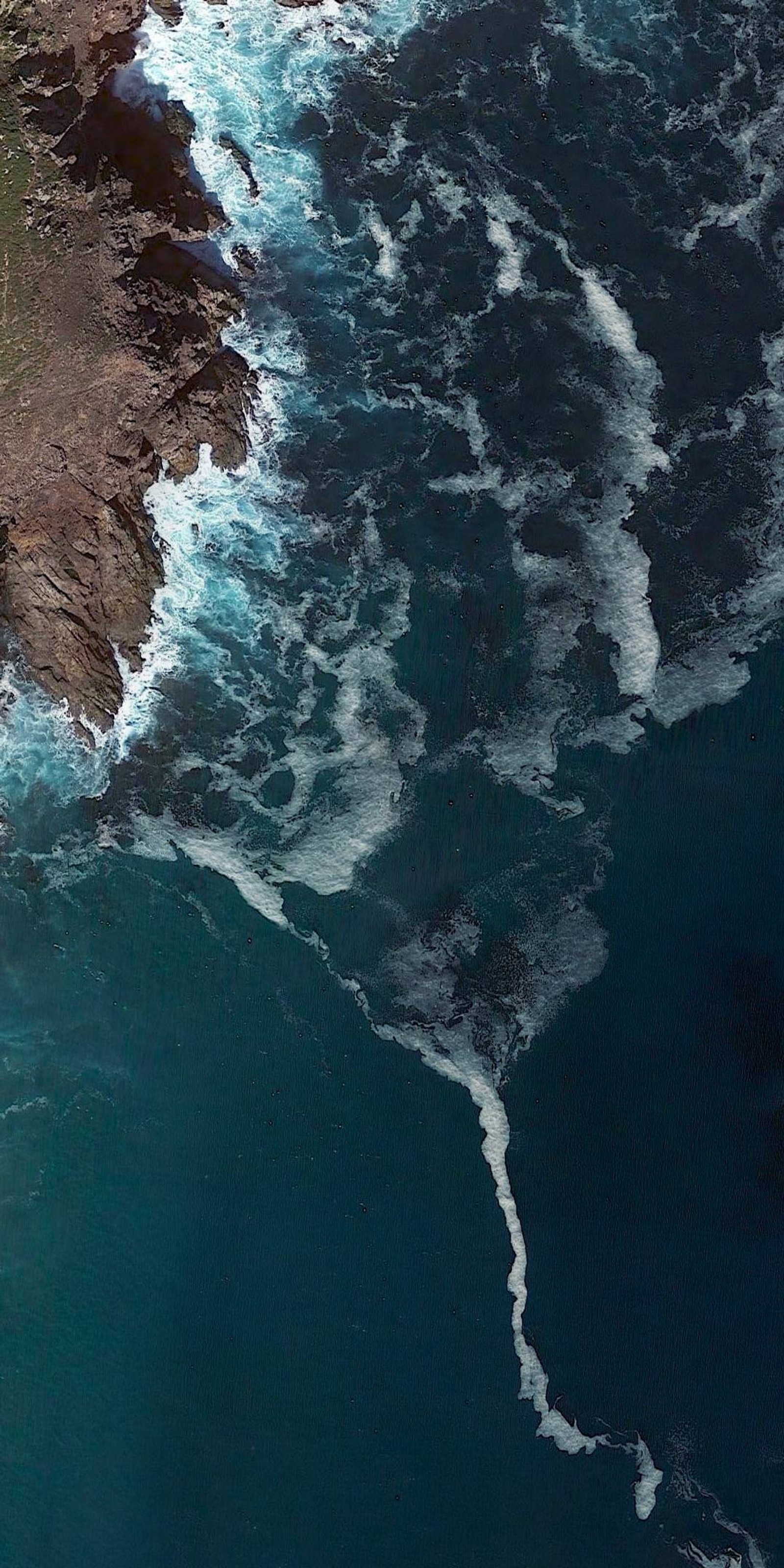 Vista aérea de un cuerpo de agua con una playa y un acantilado (océano, cascadas)