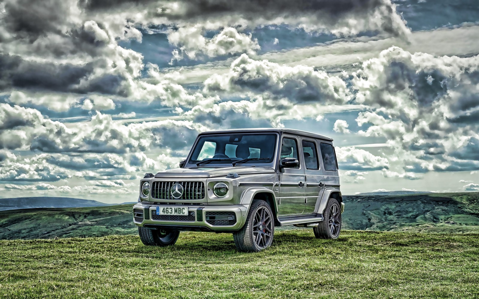 Ein bild eines fahrzeugs, das auf einem grasbewachsenen hügel mit bewölktem himmel geparkt ist (g 63, mercedes g)