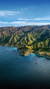 Vista aérea de montanhas acidentadas encontrando uma costa tranquila, exibindo uma paisagem natural vibrante.