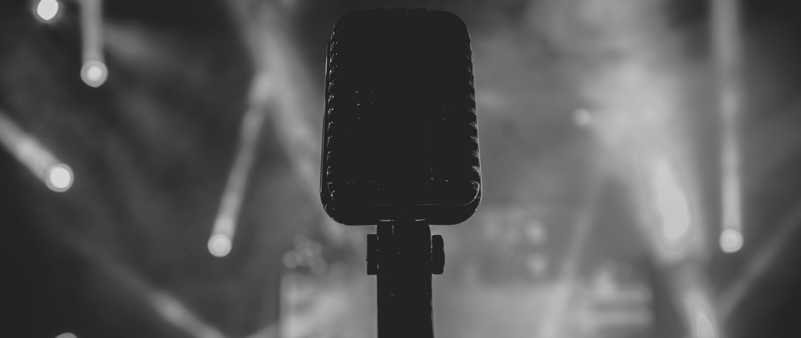 A black and white photo of a microphone in front of a stage (black, monochrome, darkness, actor, monochrome mode)