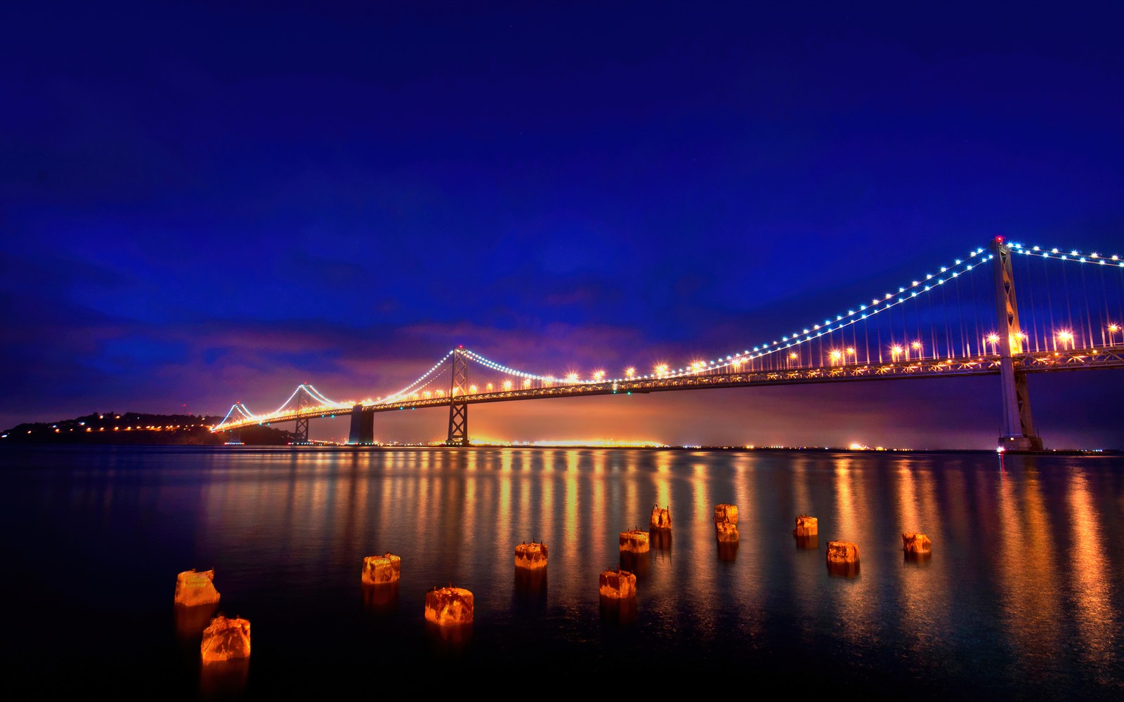 Uma vista de uma ponte iluminada à noite (ponte da baía de são francisco oakland, noite, reflexões, hora azul, frio)