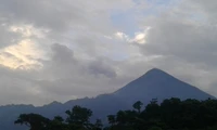 Majestoso estratovulcão se erguendo acima de uma paisagem exuberante sob um céu nublado.