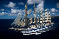 Majestic tall ship sailing under full sail against a backdrop of blue skies and ocean waves.