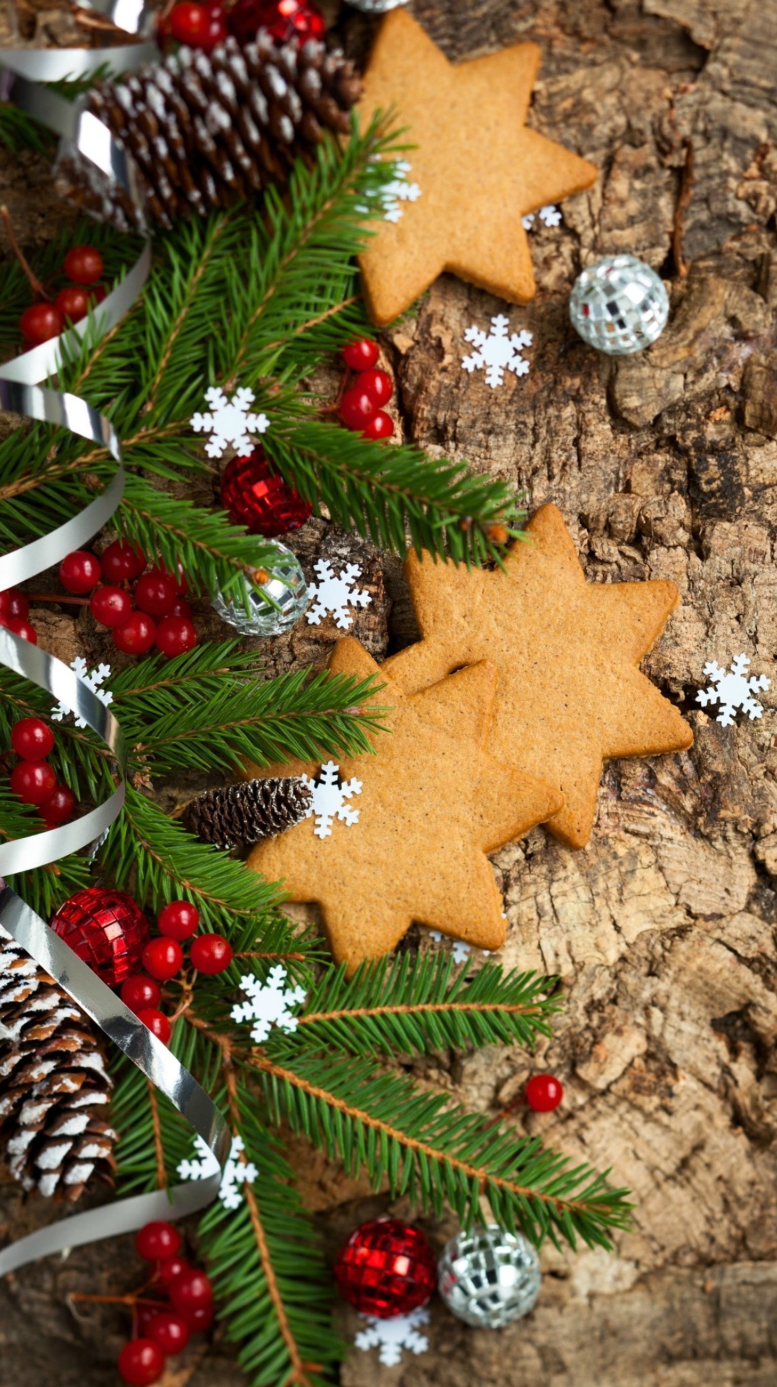 Há dois biscoitos e decorações em um tronco de árvore (decorações de natal, cone, pão de gengibre, estrelas)