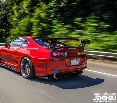 Tomada dinâmica de um carro esportivo vermelho modificado em movimento em uma rodovia.