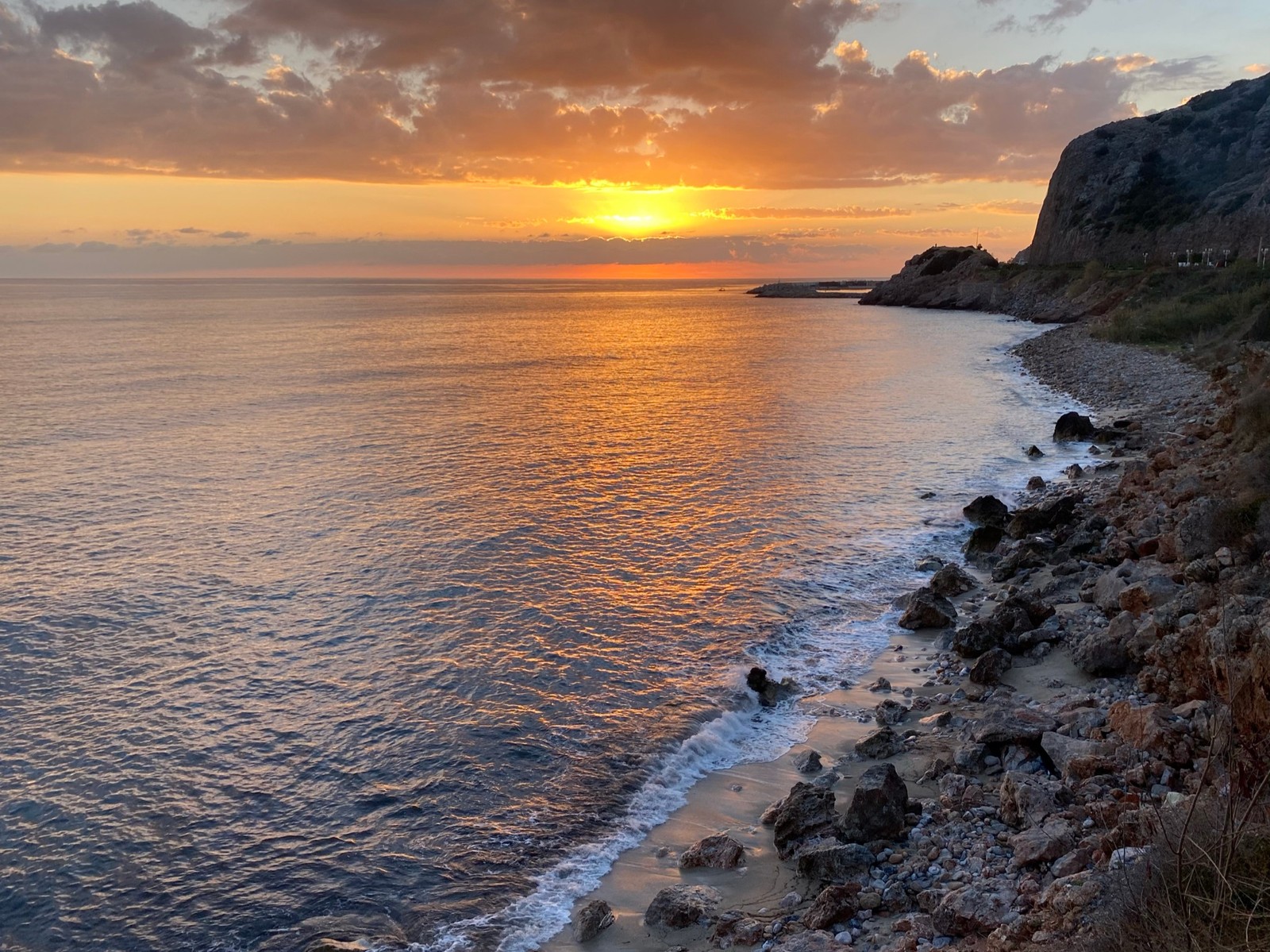 Sunset over the ocean with a rocky shore and a beach (coast, water, cloud, water resources, ecoregion)