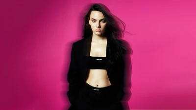 Dafne Keen in a stylish black outfit against a vibrant pink background.