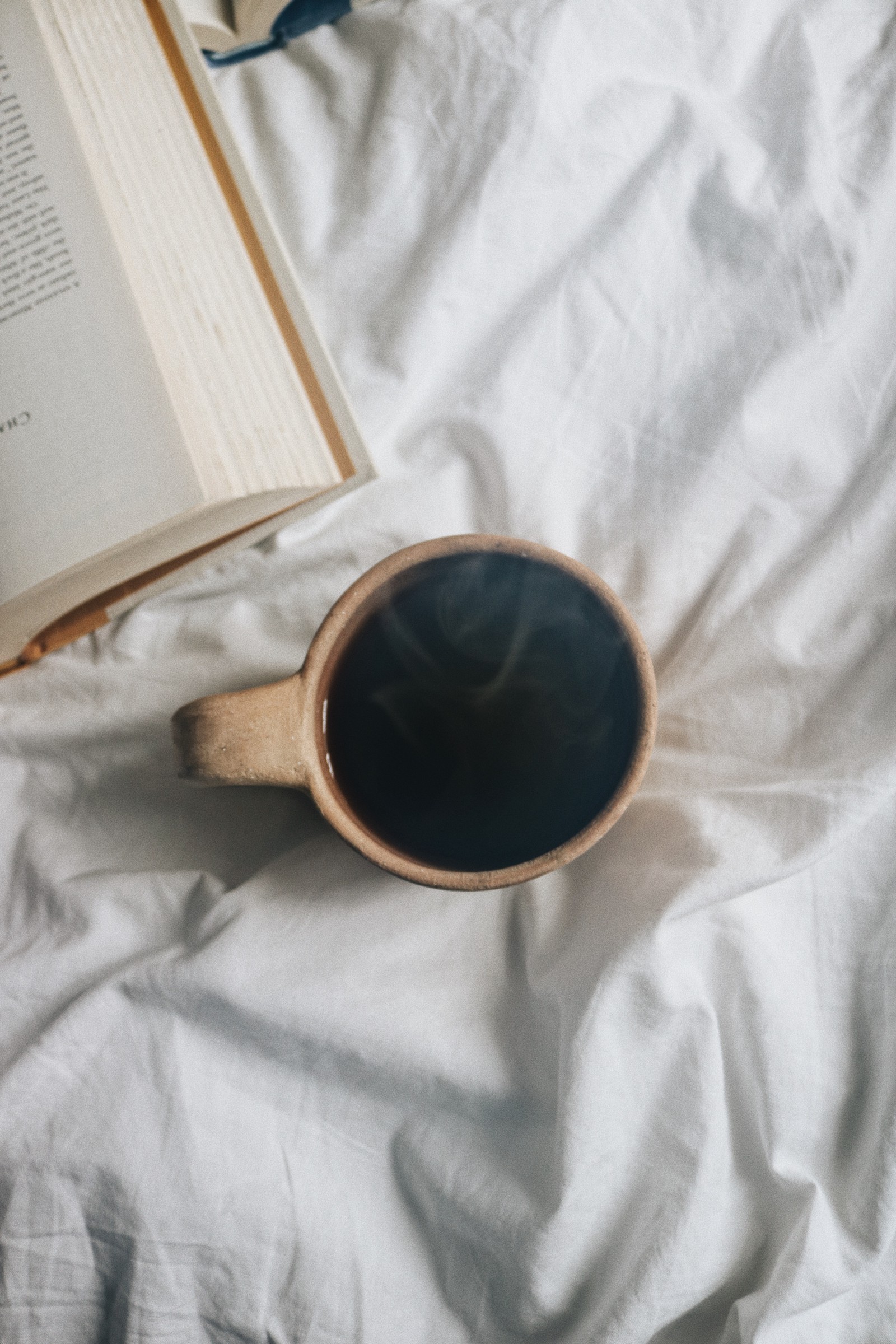 There is a cup of coffee and a book on a bed (eyewear, metal, coffee, vision care, sunglasses)