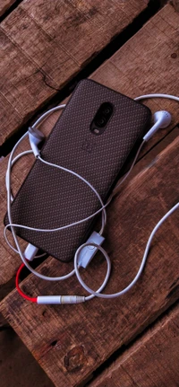 A mobile phone tangled in earphones on a wooden surface.