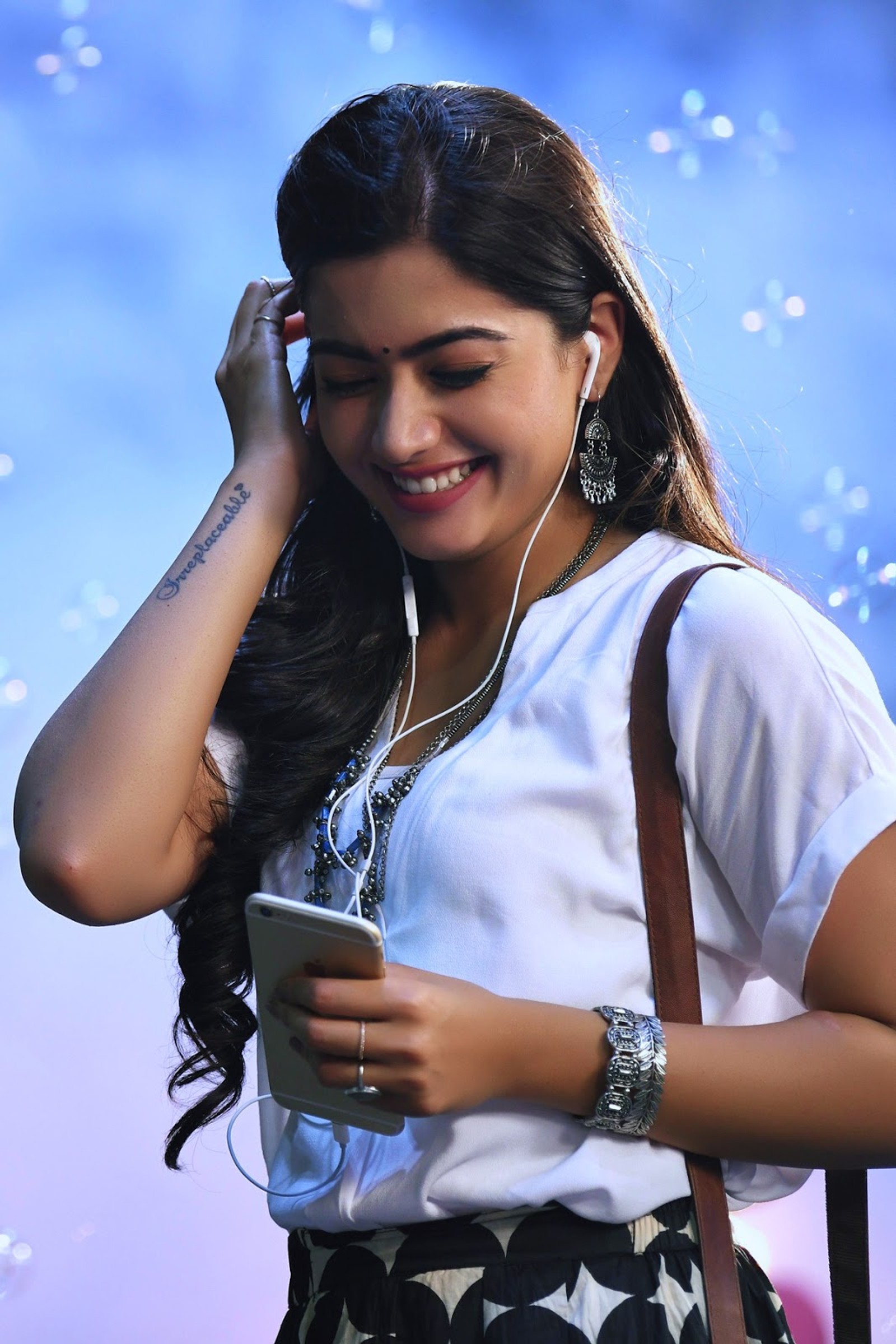 Una mujer sonriente con auriculares y un bolso usando una tableta (actriz, lindo, rashmika, rashmika mandanna, rashmika mandana)