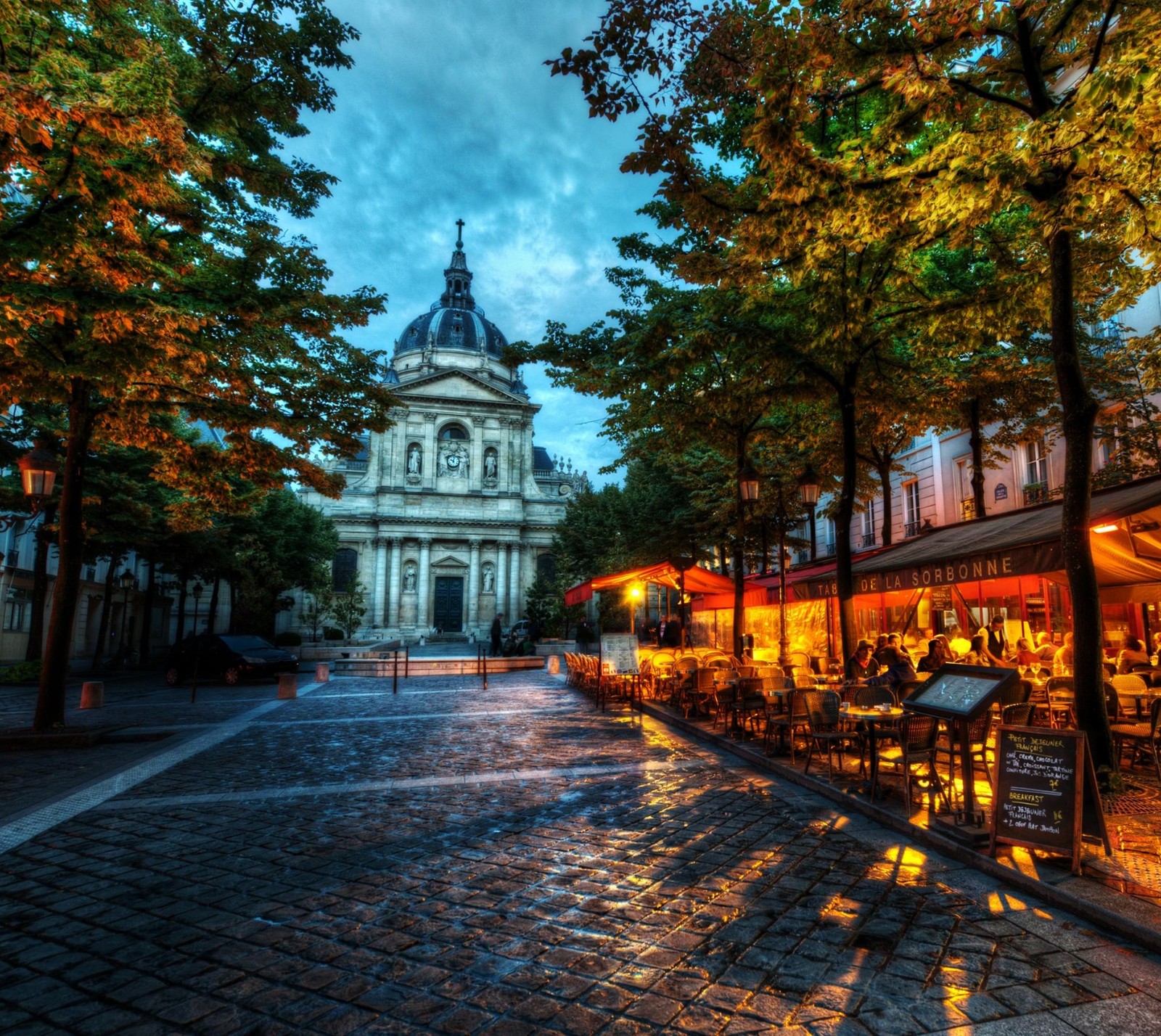 Arafed view of a street with tables and chairs and a church in the background (france, landscape, road, sorbonne, town)