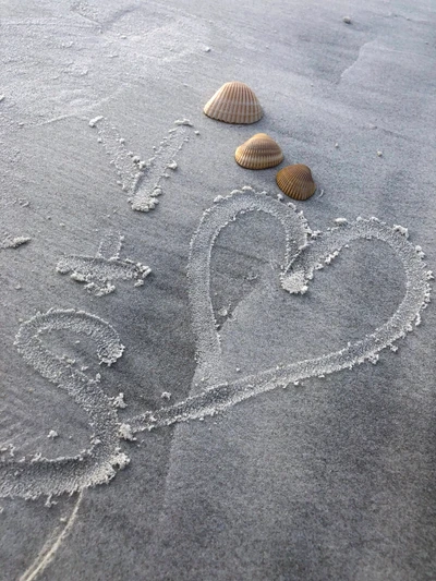 Herz im Sand mit Muscheln an einem grauen Strand