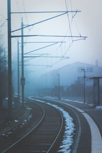 Foggy Morning at the Train Station with Curving Tracks and Overhead Power Lines