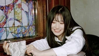 Song Ha Young do fromis_9 irradia alegria enquanto segura um acessório de renda, emoldurada por uma colorida janela de vitral.