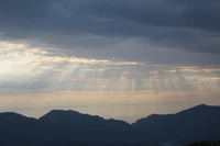 Radiant Sunlight Breaking Through Clouds Over a Mountain Range at Dusk