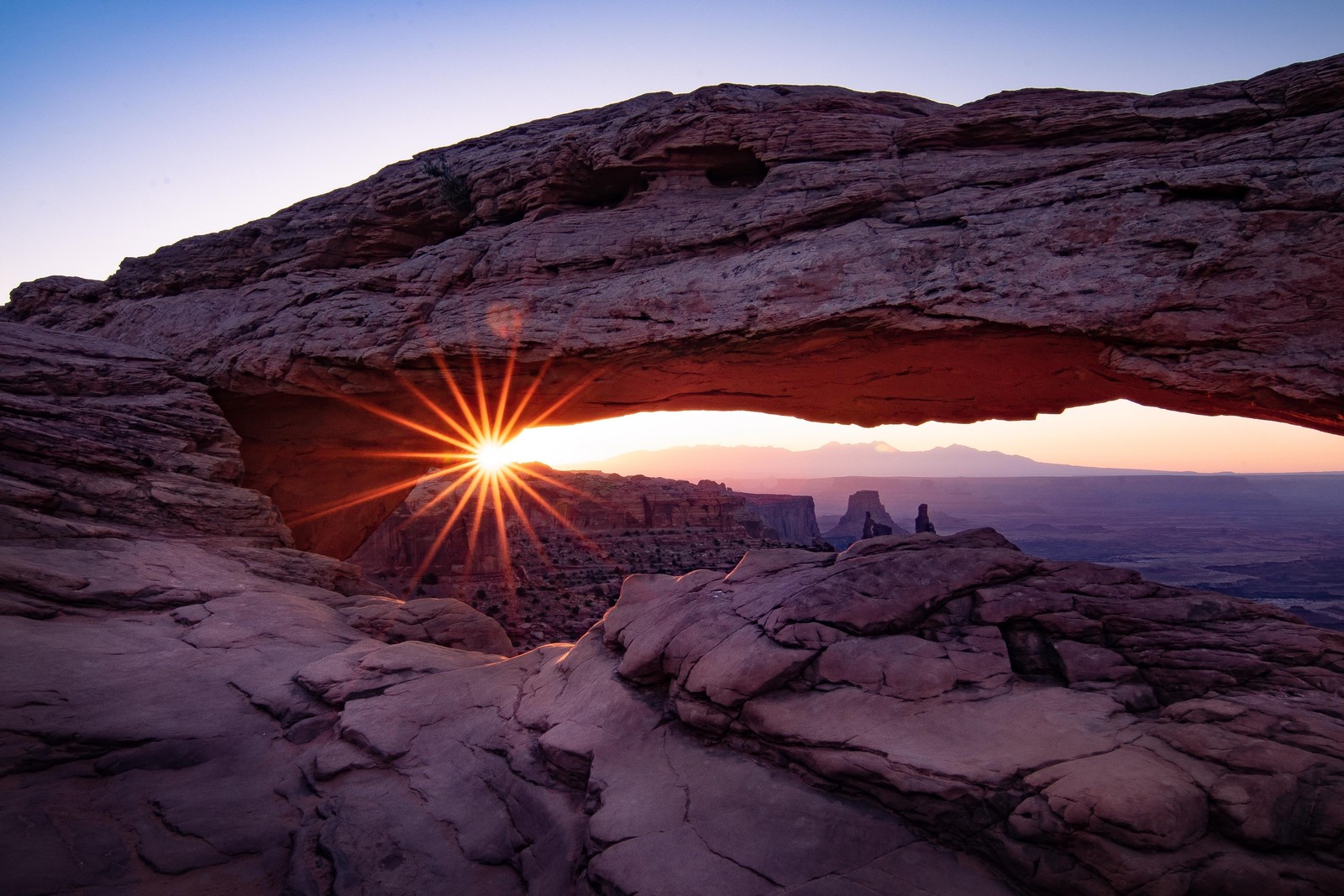 A close up of a rock formation with a sun setting in the background (mesa arch, arches national park, national park, park, formation)