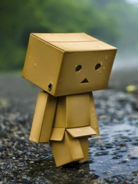 A lonely cardboard figure walks down a rain-soaked path, embodying solitude and sadness.