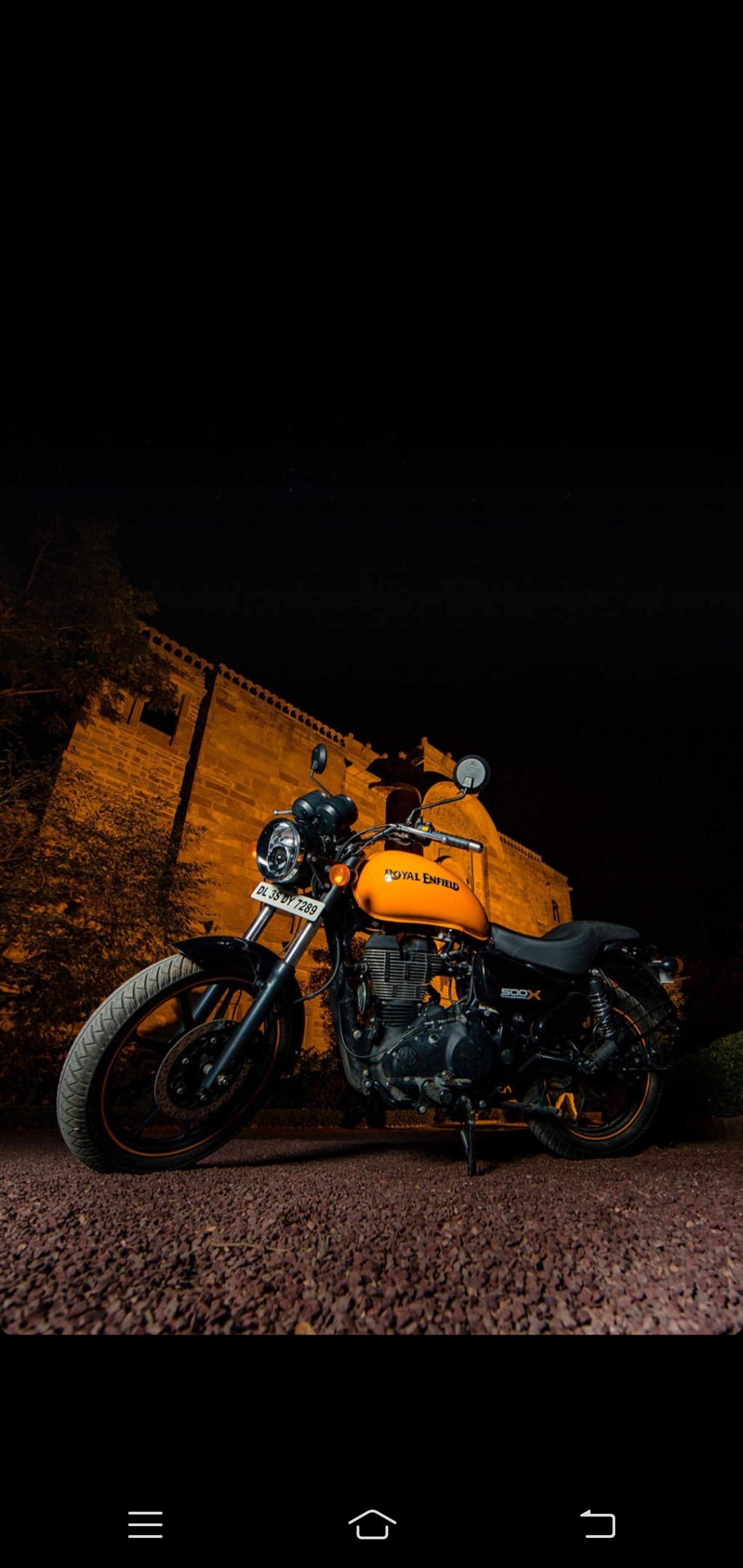 There is a motorcycle parked in front of a brick building (re, royal, royal enfield)