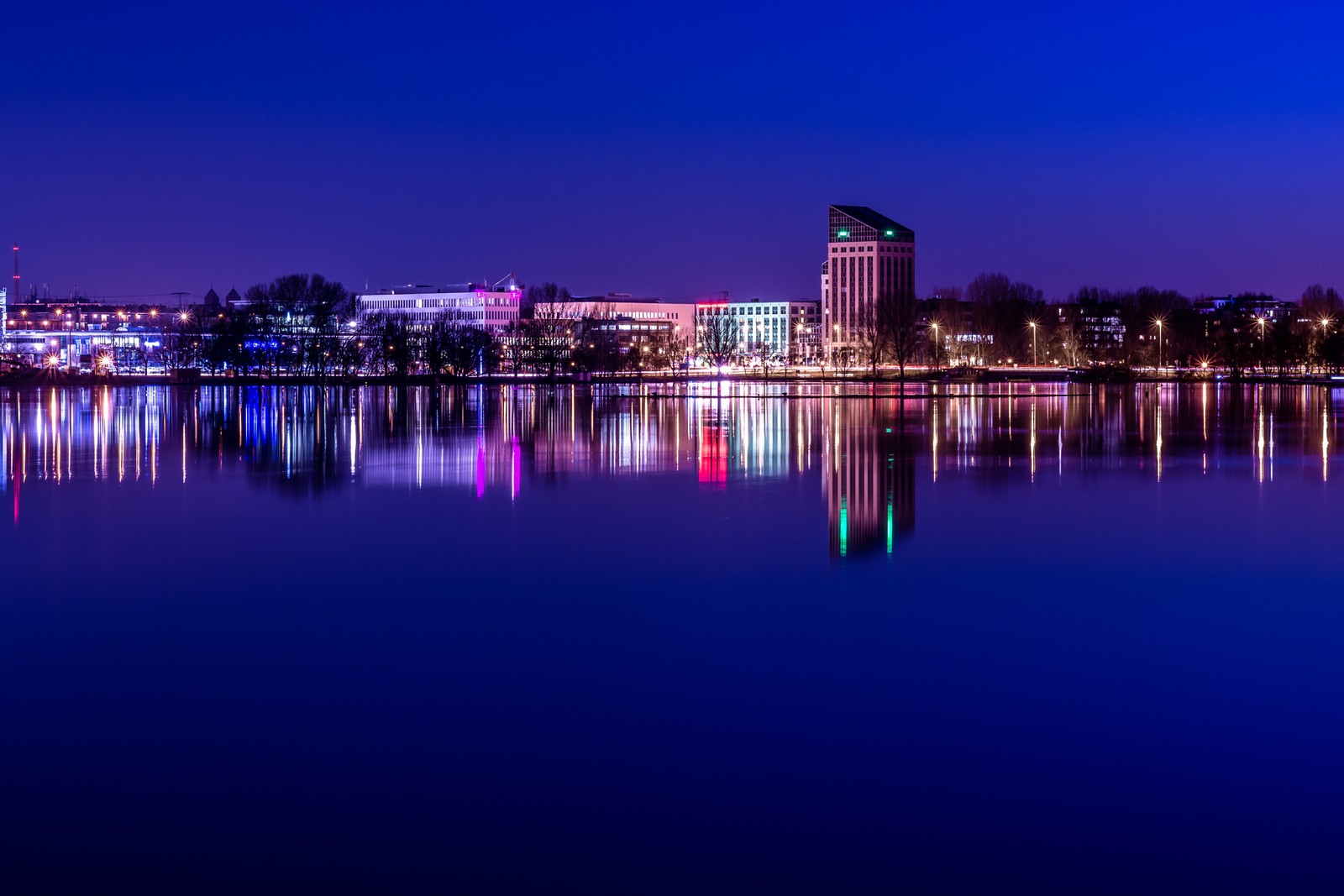 Vista aérea de um horizonte urbano à noite com um lago em primeiro plano (panorama, noite, reflexo, azul, cidade)