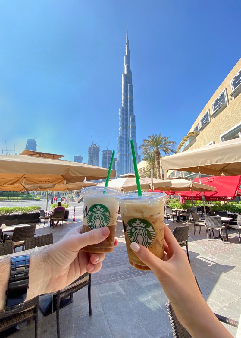 Кто-то держит две чашки кофе starbucks перед высоким зданием (дубай, dubai, аэрокосмическая инженерия, садовая мебель, башня)