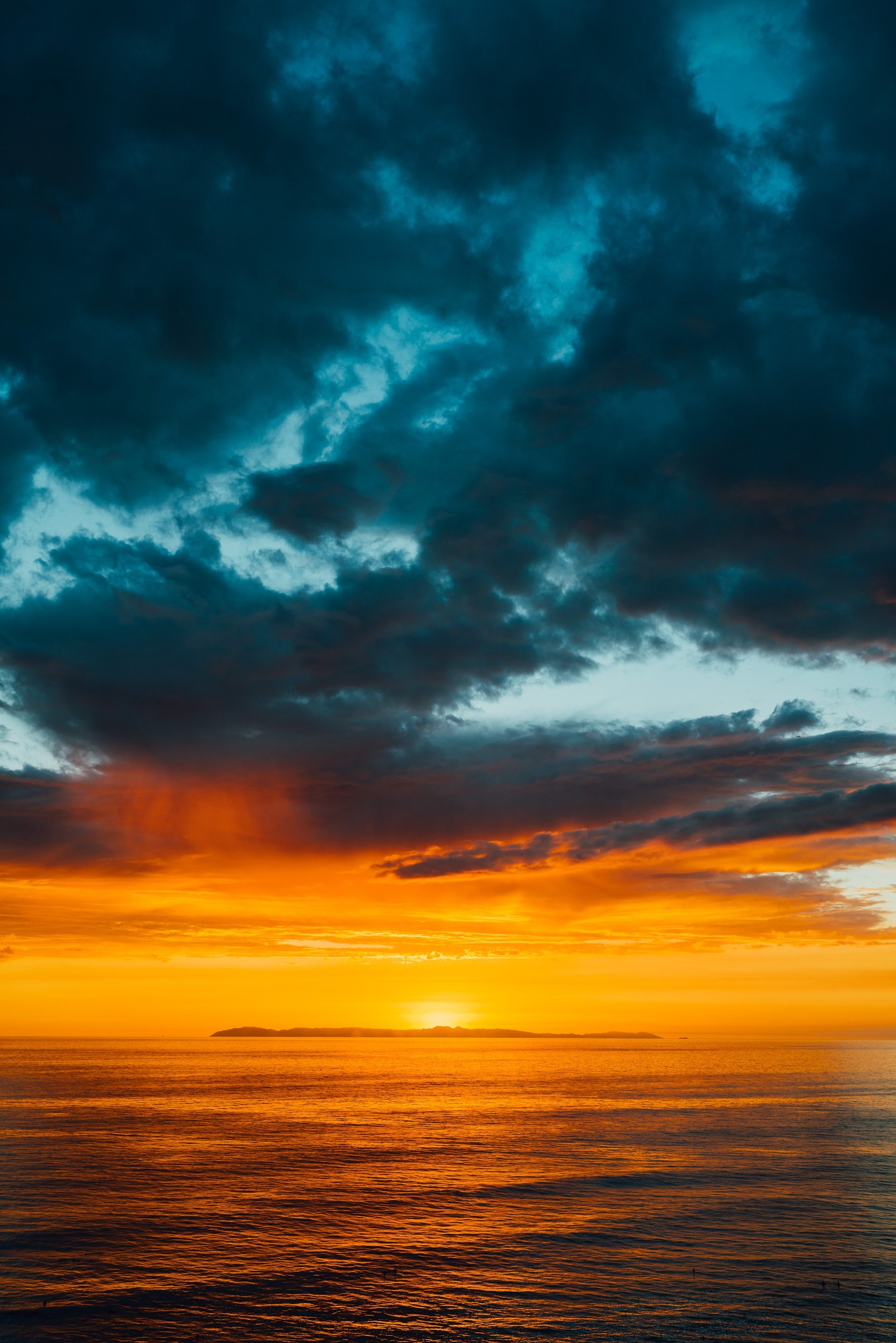 Vue aérienne d'un coucher de soleil sur l'océan avec un bateau dans l'eau (nuage, bleu, bleu vert, orange, jaune)