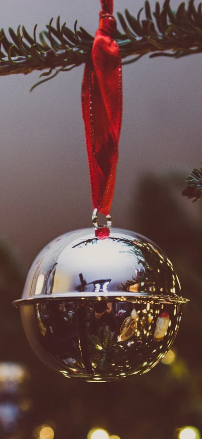 Glänzende silberne Weihnachtsornament, das von einem Baumzweig hängt und Feiertagslichter und Grün reflektiert.