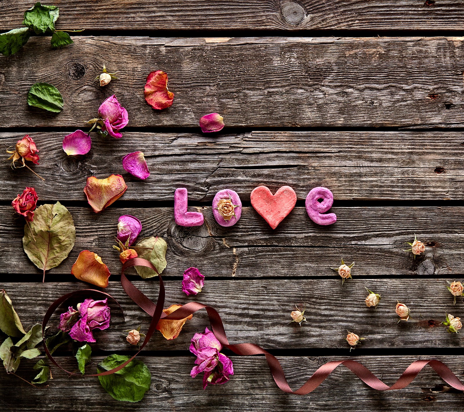 Flowers and leaves are arranged around the word love on a wooden surface (love, petals, romance, rose, wood)