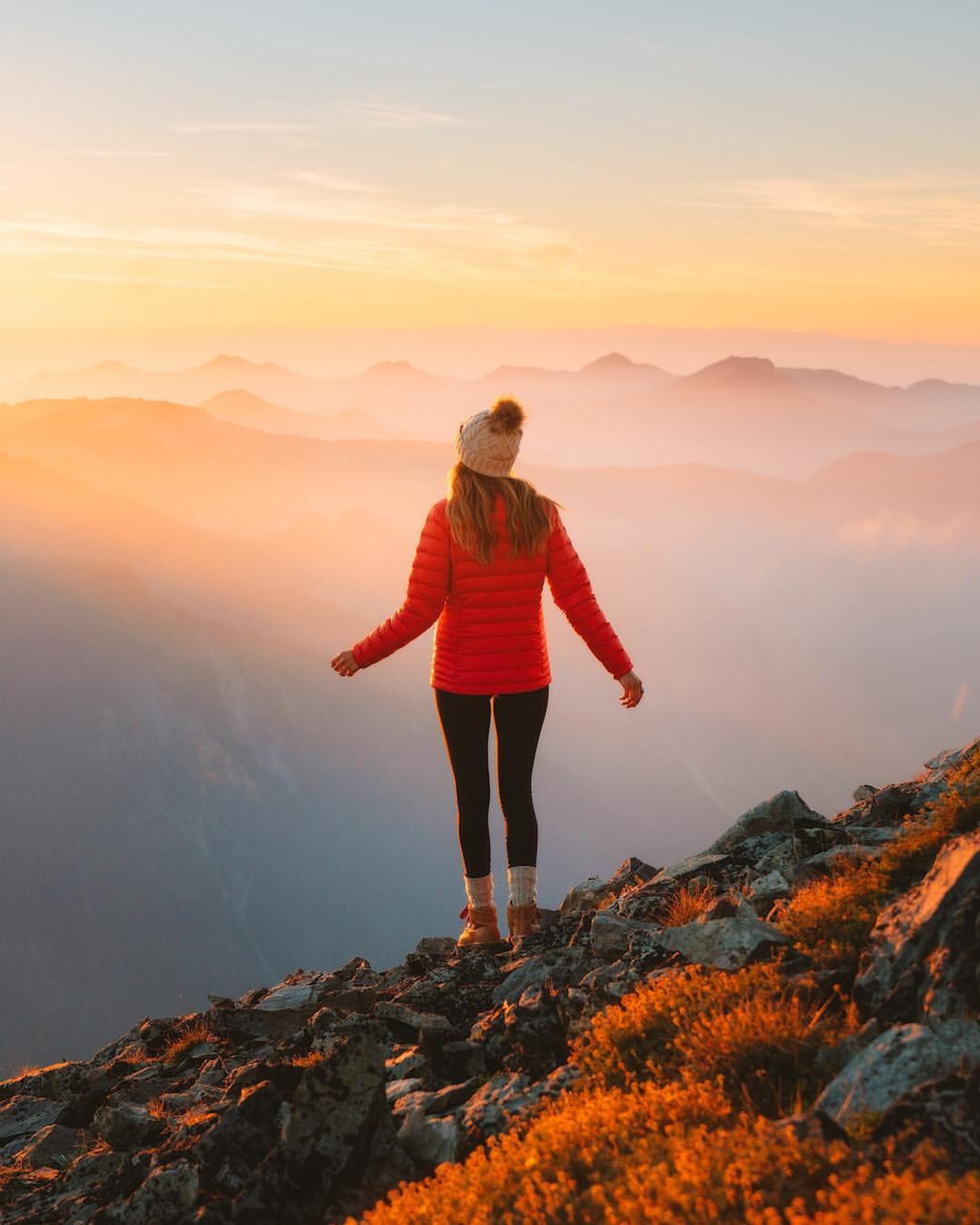 Eine frau, die auf einem berggipfel steht und auf die berge schaut (mädchen, frau, leute, the view, natur)