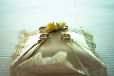 Elegant wedding rings displayed on a decorative pillow adorned with a yellow flower and lace, symbolizing love and commitment.