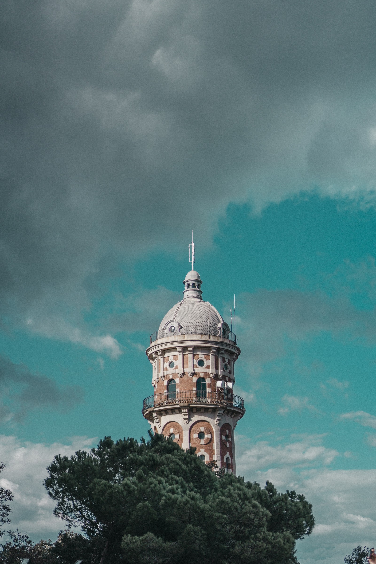 Hay una torre alta con un reloj en la parte superior (árbol, edificio, cielo, hito, barcelona)