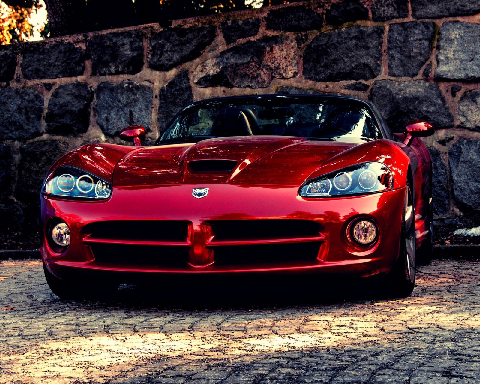 Un primer plano de un coche deportivo rojo estacionado frente a una pared de piedra (dodge, raza, coche rojo, velocidad, víbora)