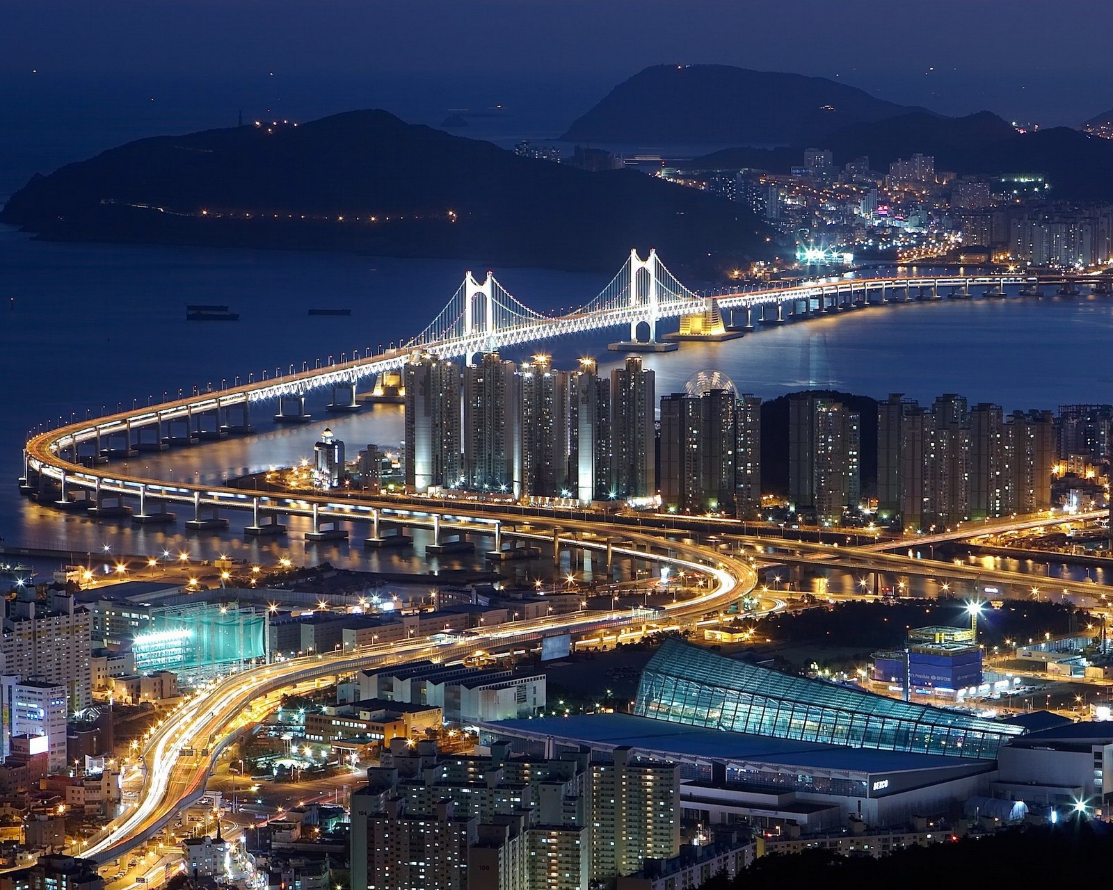 Una vista de la ciudad de noche con un puente y un río (puente, ciudad)