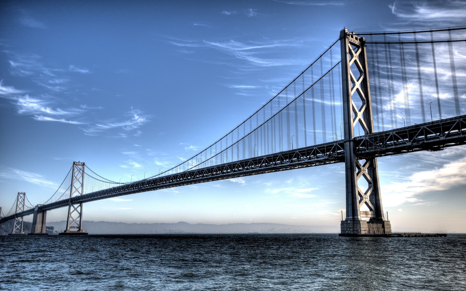 Uma vista árabe de uma ponte que se estende sobre a água com um fundo de céu (ponte da baía de oakland, oakland bay bridge, ponte golden gate, golden gate bridge, ponte)